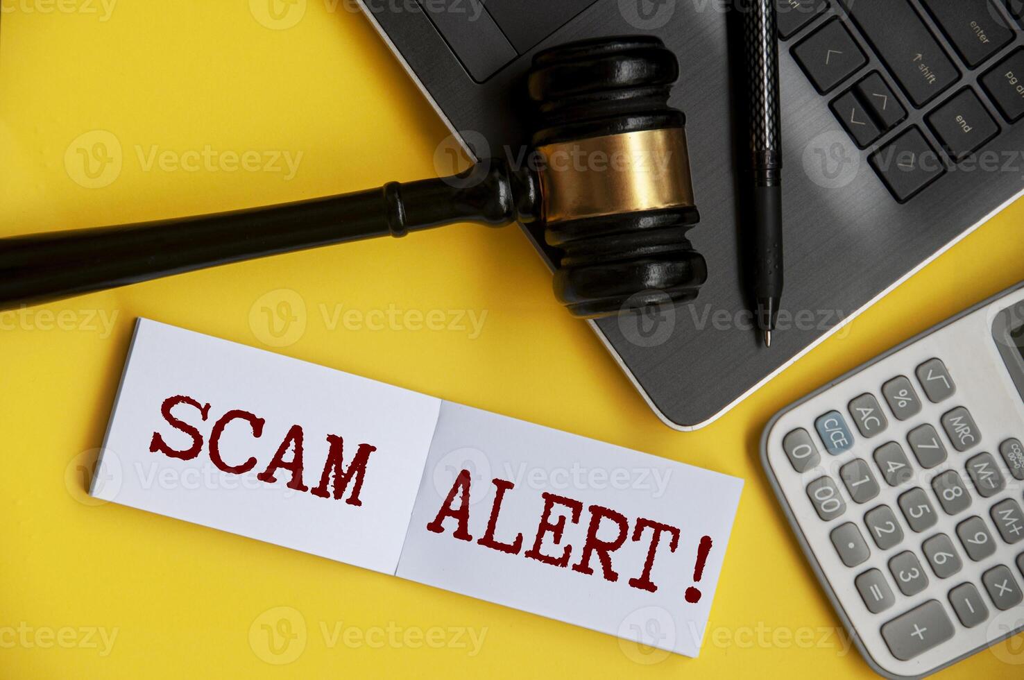 Scam alert text on notepad with gavel, laptop, pen and calculator background. Security concept photo