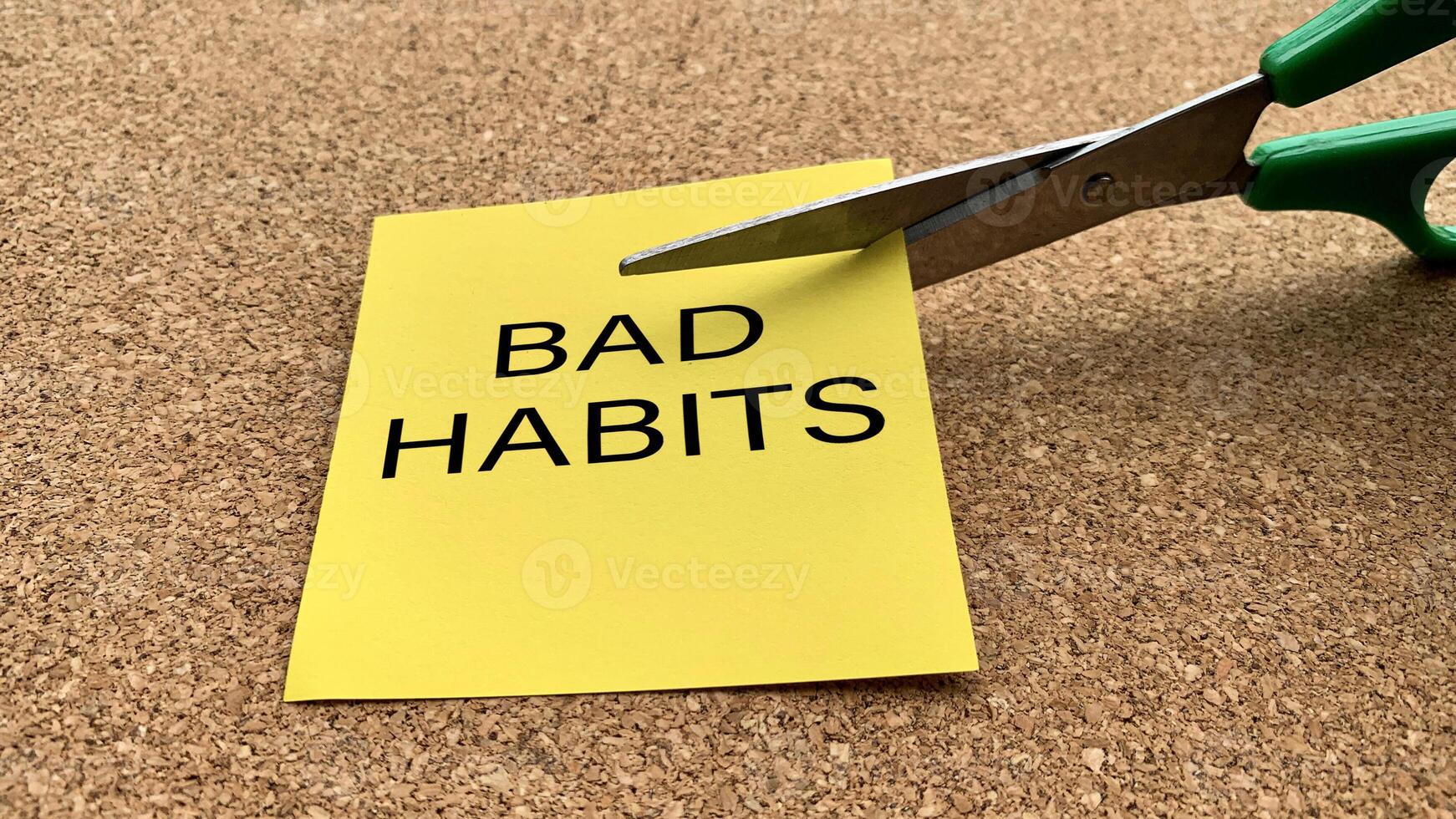 Scissors that cut yellow notepad with bad habits text on a wooden desk background. Spending concept photo