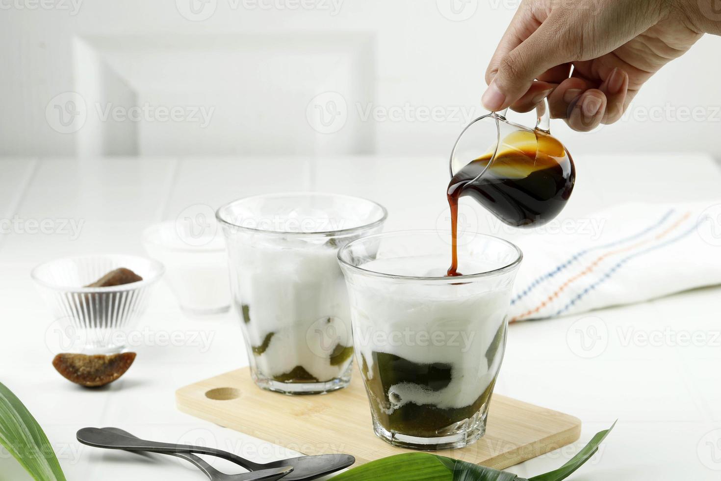 vierta azúcar de palma líquida en el vaso con bebida de gelatina de hierba verde o cingcau hijau. foto