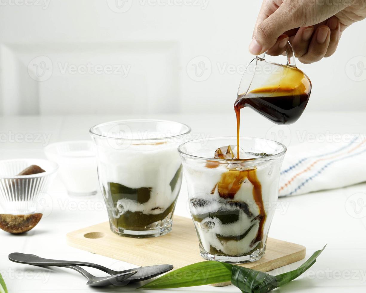 vierta azúcar de palma líquida en el vaso con bebida de gelatina de hierba verde o cingcau hijau. cincau ijo es comida callejera popular de indonesia foto