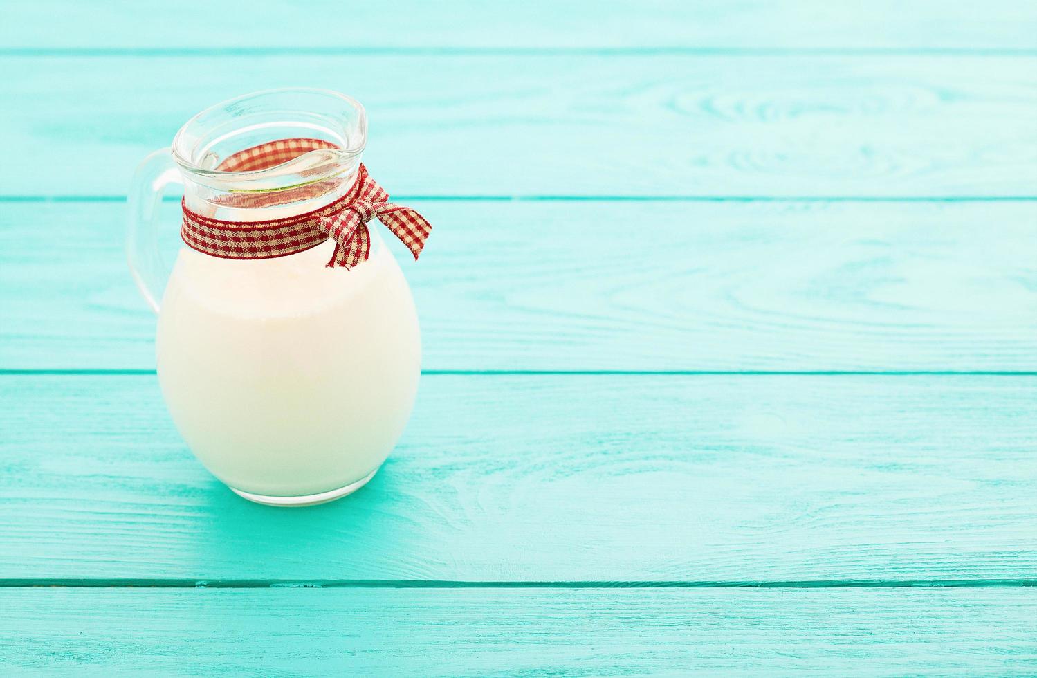 Lunch time with jug of milk and plaid ribbon on blue wooden background. Top view and copy space. Selective focus photo