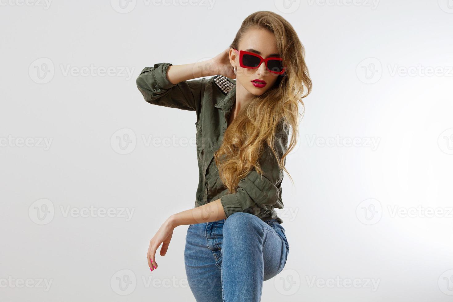Stylish woman in red glasses looking at camera at studio isolated on white background. Copy space. Trendy style of beautiful luxury model with red lips makeup. Long wavy shiny blonde hair photo