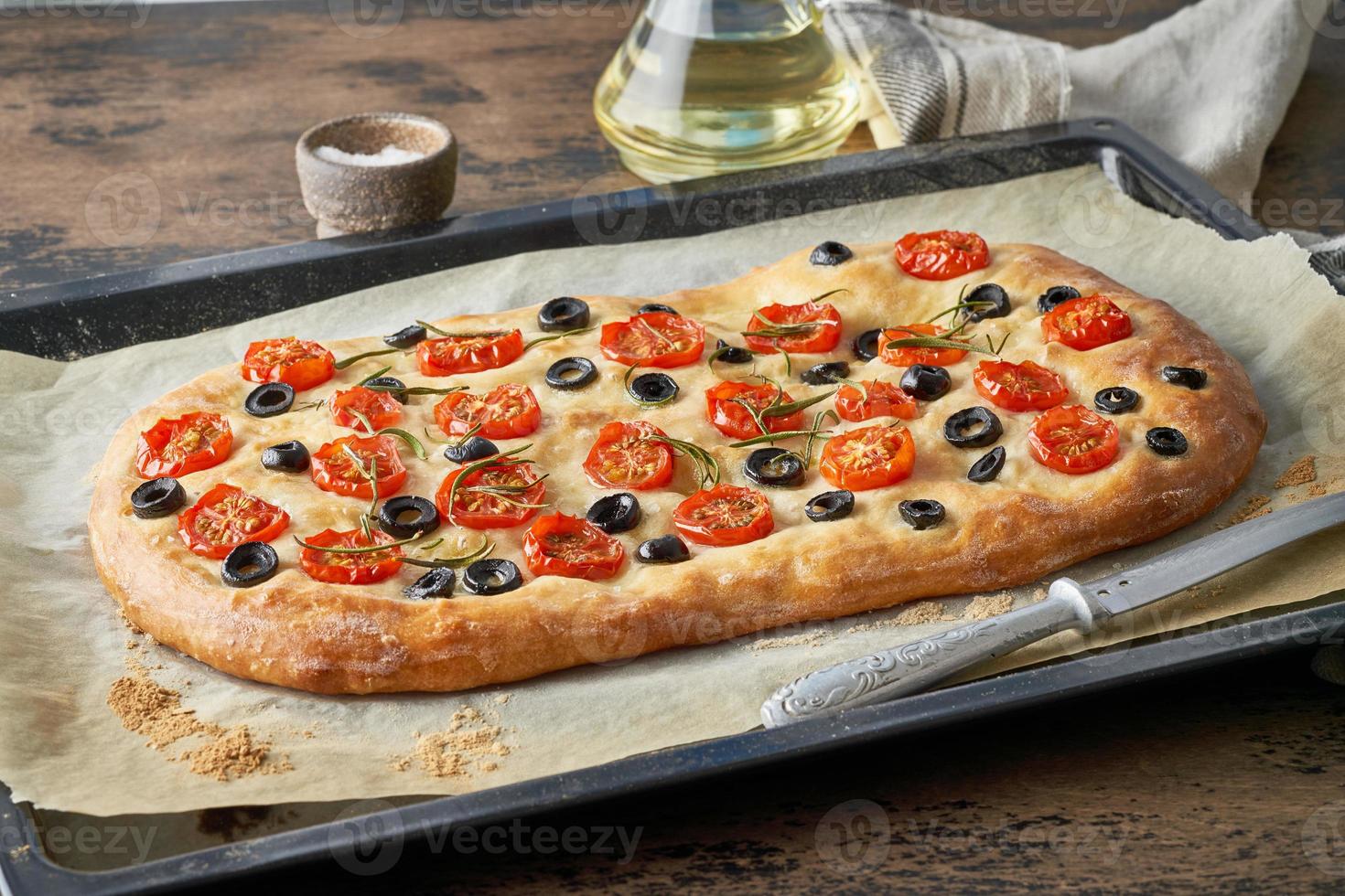 focaccia, pizza, pan plano italiano con tomates, aceitunas y romero en bandeja foto
