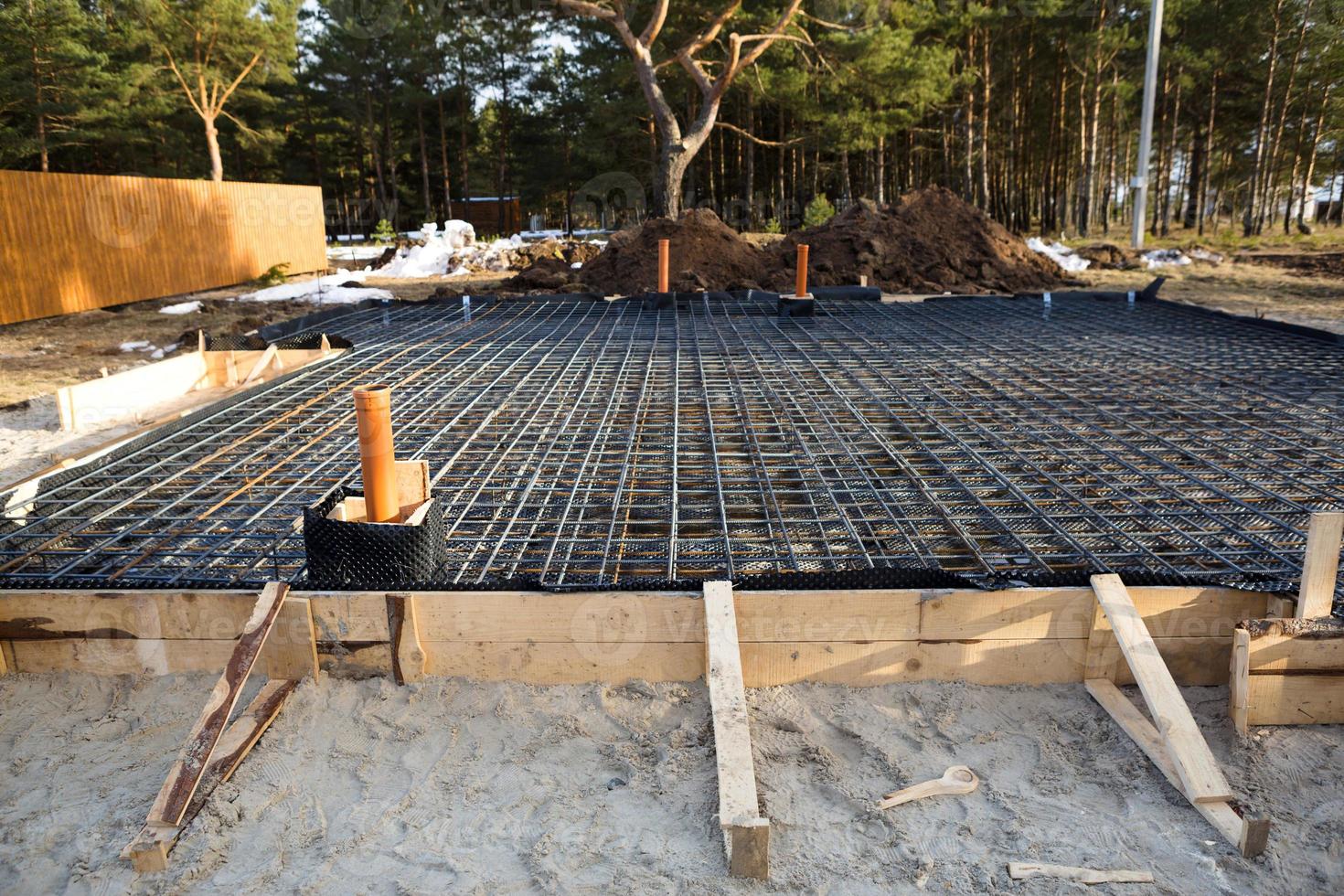 Iron fittings on a wooden blind area with laid pipes are the basis for pouring the foundation of the house with a concrete slab. Construction of cottages, design, engineering communications. photo