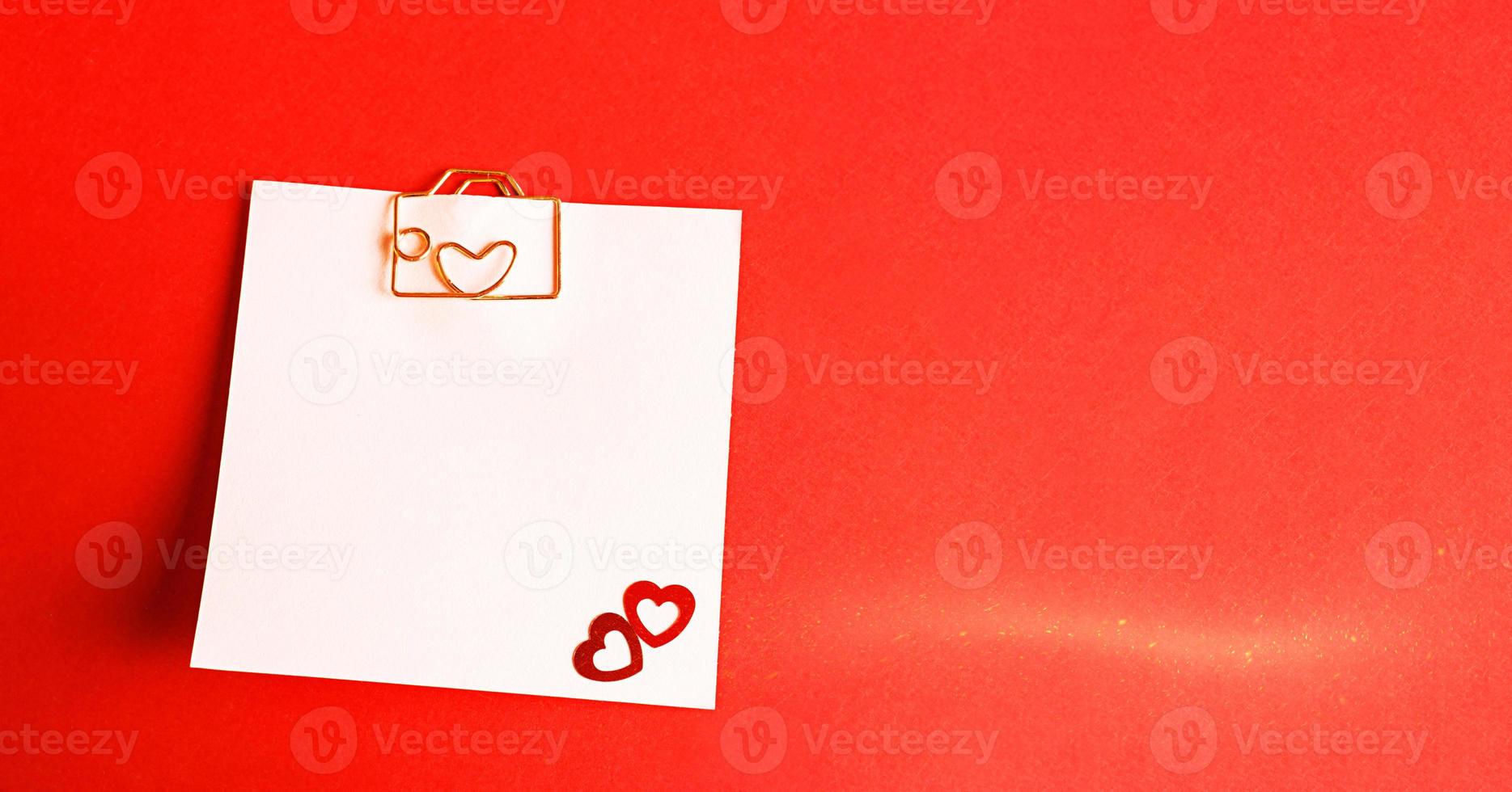 Square sheet for notes with a paper clip in shape of a letter and a heart. Decor of couples in love with hearts on a red background. Valentine's Day, message, greeting, declaration of love. Copy space photo