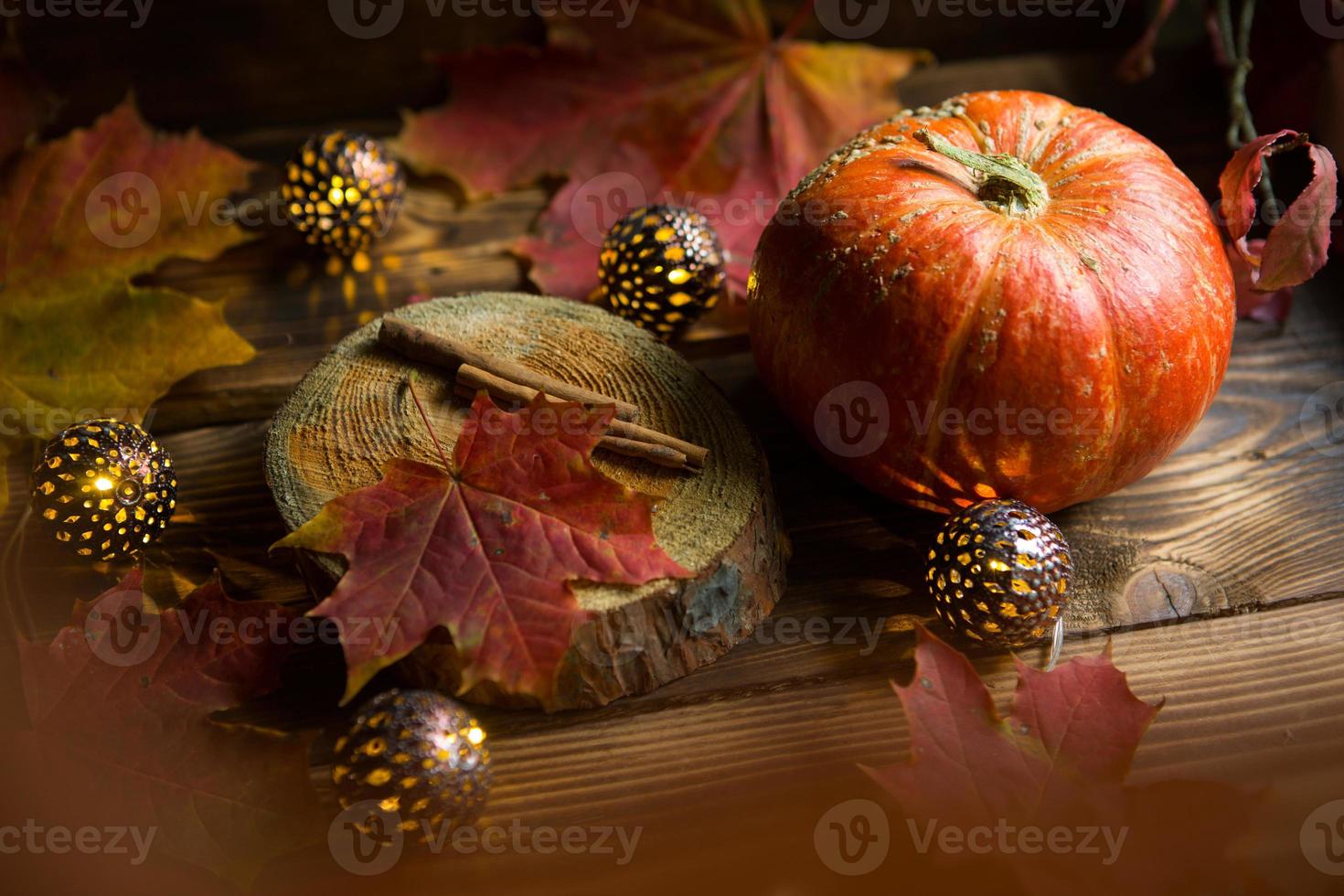 Orange natural round pumpkin on a wooden table with fallen yellow and red maple leaves, cinnamon sticks. Lights garlands, warm autumn atmosphere, thanksgiving, harvest festival, Halloween. Copy space photo