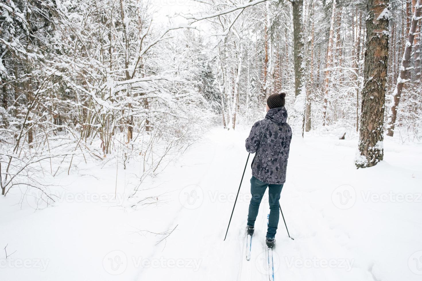 esquiador con sombrero con pompón con bastones de esquí en las manos con la espalda contra el fondo de un bosque nevado. esquí de fondo en el bosque de invierno, deportes al aire libre, estilo de vida saludable. foto