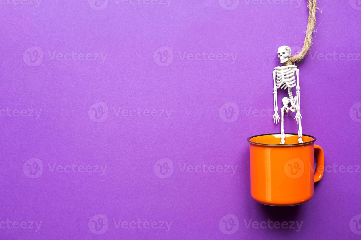 Orange mug on a purple background with terrible Halloween decorations. The concept of the Halloween holiday. Drink, fun, party. Copy space, mock up, flatly photo