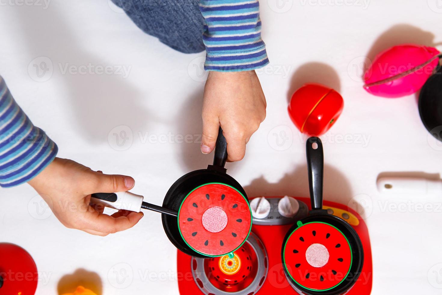 The child plays with sliced plastic vegetables and fruits with Velcro, cooks food on a toy stove in a bowl. Children's cooking, a girl learns to cook. White background, close-up, concept. photo