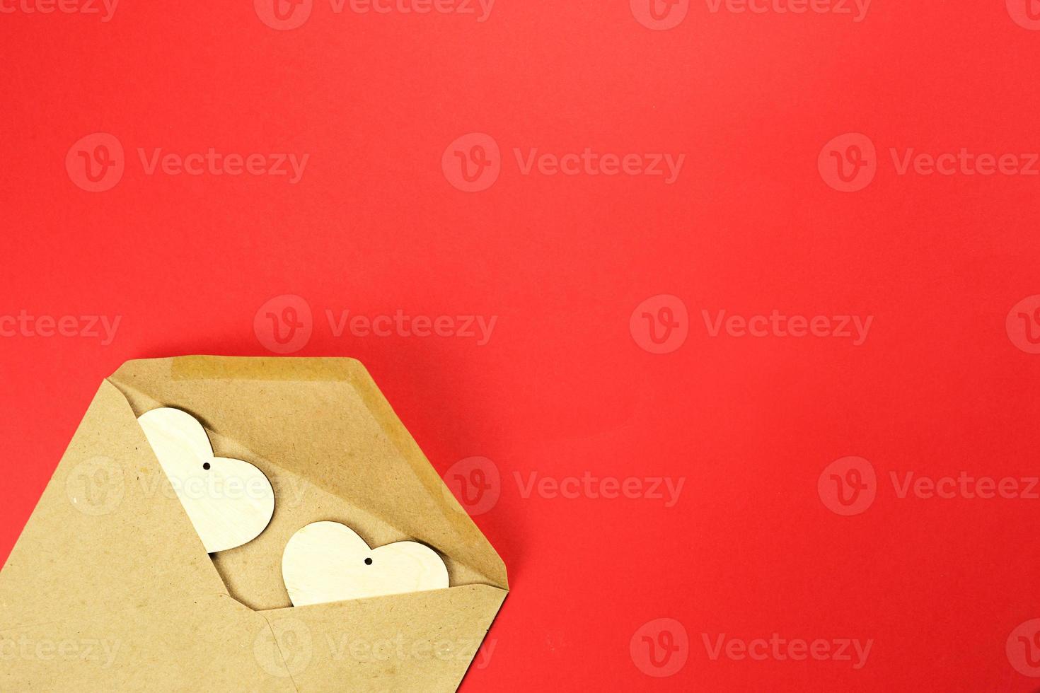 Wooden hearts spill out of an open envelope on a red background. Valentine's Day, love letter, declaration of love, acquaintance. Copy space, mock up photo