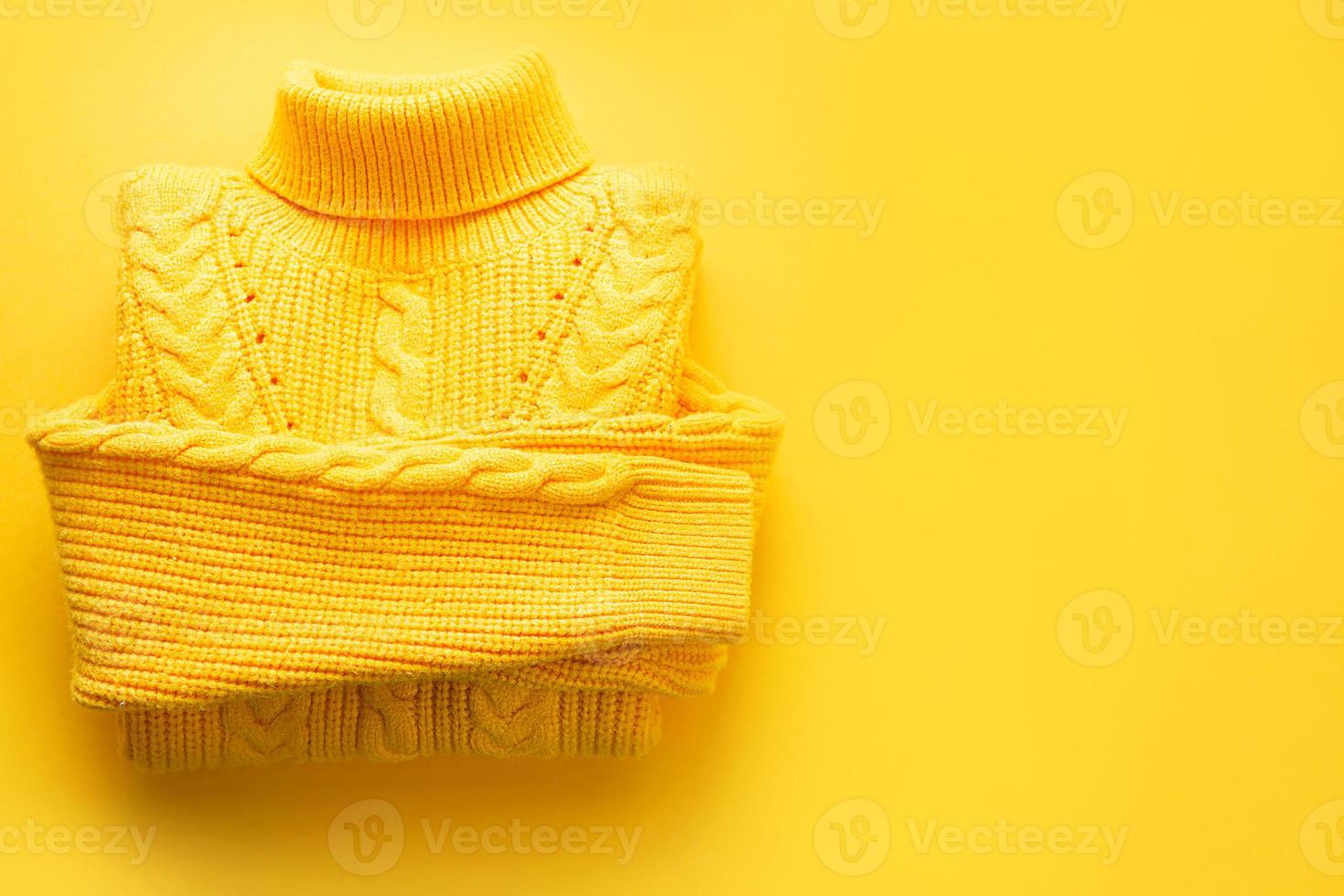 A yellow knitted sweater is rolled up on a yellow background, copyspace. Warm seasonal clothing for spring and autumn, lifting the mood photo