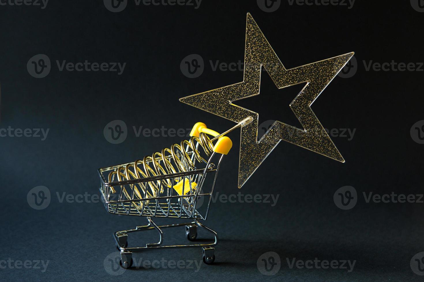 Shopping cart with a gold transparent star with sequins in the shape of a Christmas tree on a black background. Black Friday, buying gifts for the new year. Space for text photo