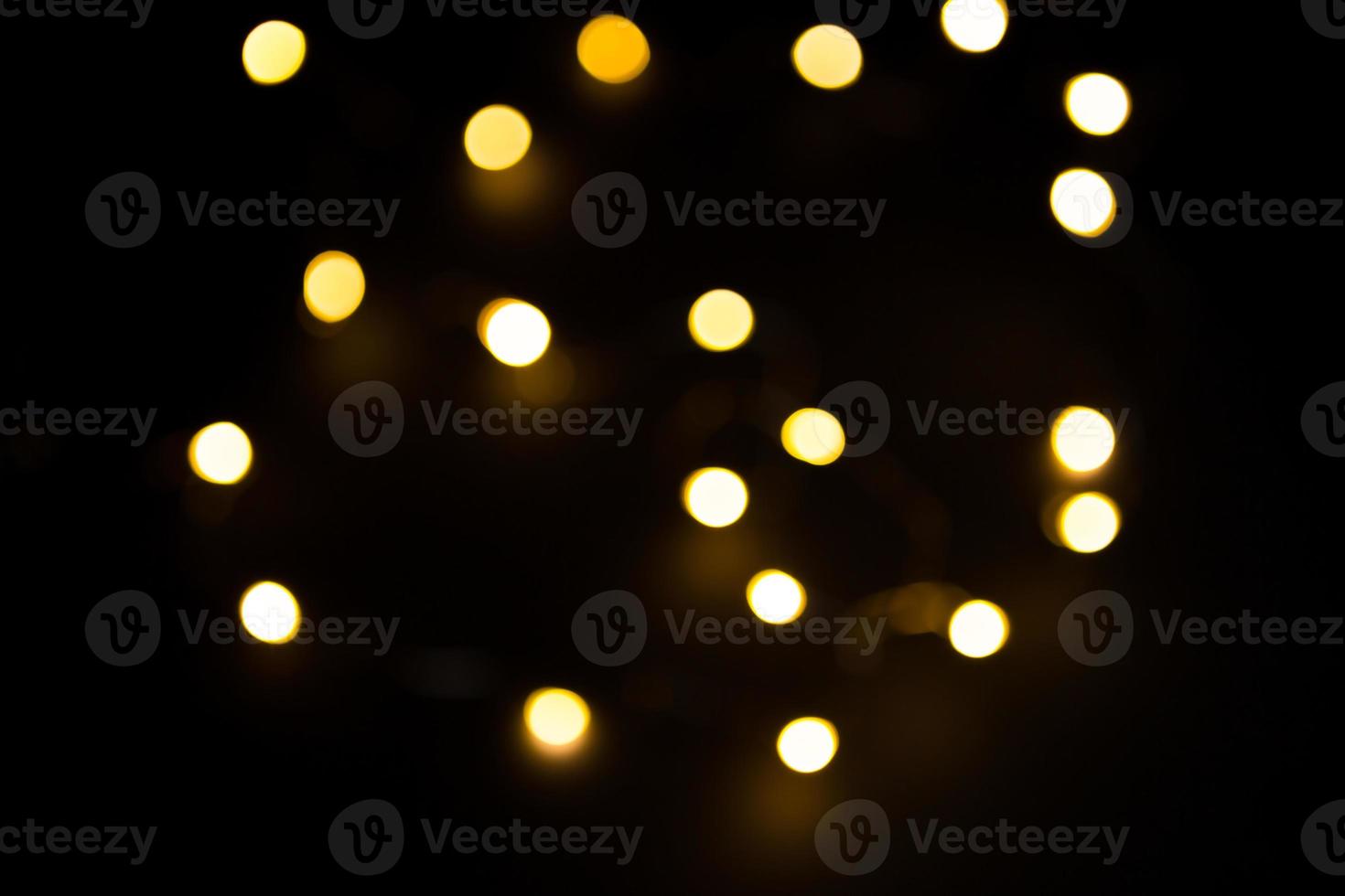 Yellow and gold lights garland in a blur on a black background. Bokeh of flying circles in the defocus. Festive atmosphere of Christmas and new year. Celebrate background photo
