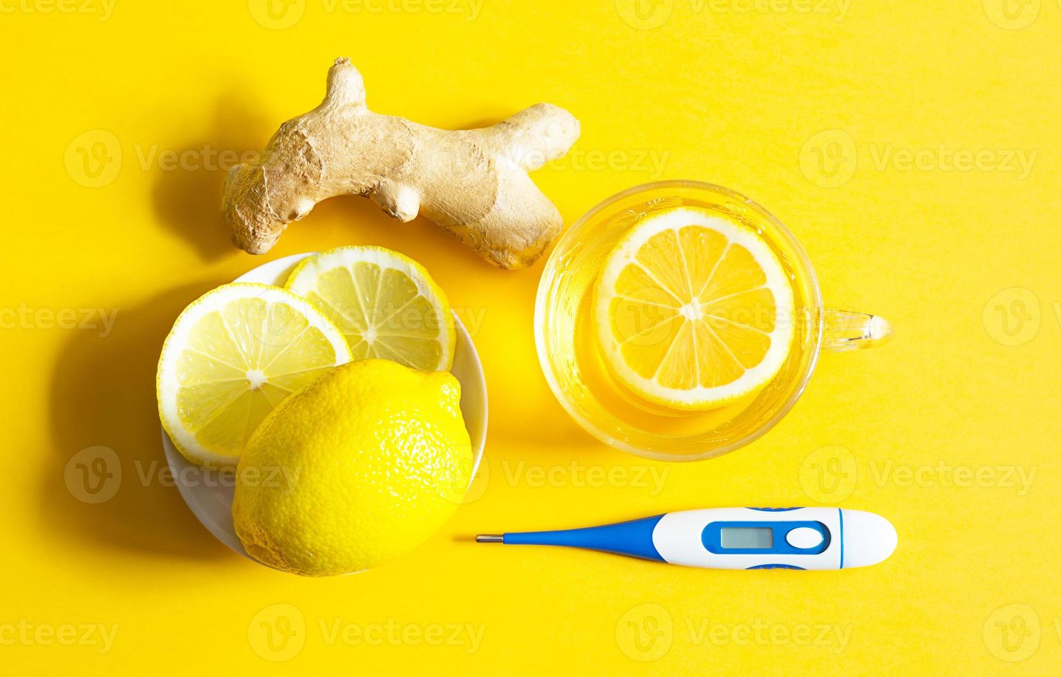 Medicinal tea in cup, ginger, lemon-strengthen immune system in the cold season. Vitamin drink for health and ingredients, thermometer on a yellow background. Flu, cold, immunity, fever, antipyretic photo
