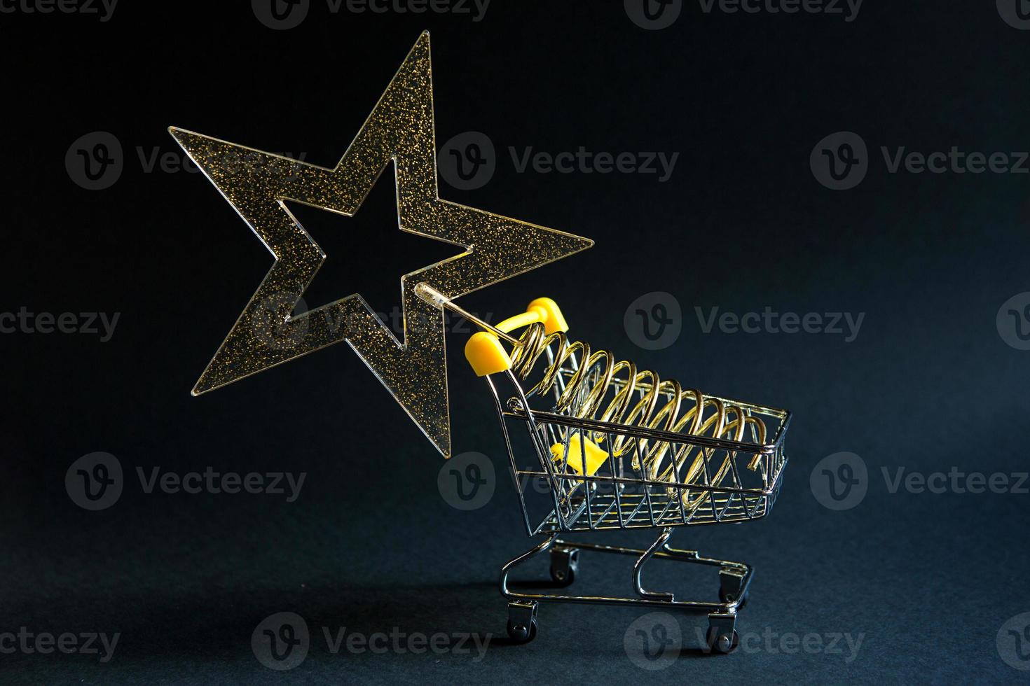 Shopping cart with a gold transparent star with sequins in the shape of a Christmas tree on a black background. Black Friday, buying gifts for the new year. Space for text photo