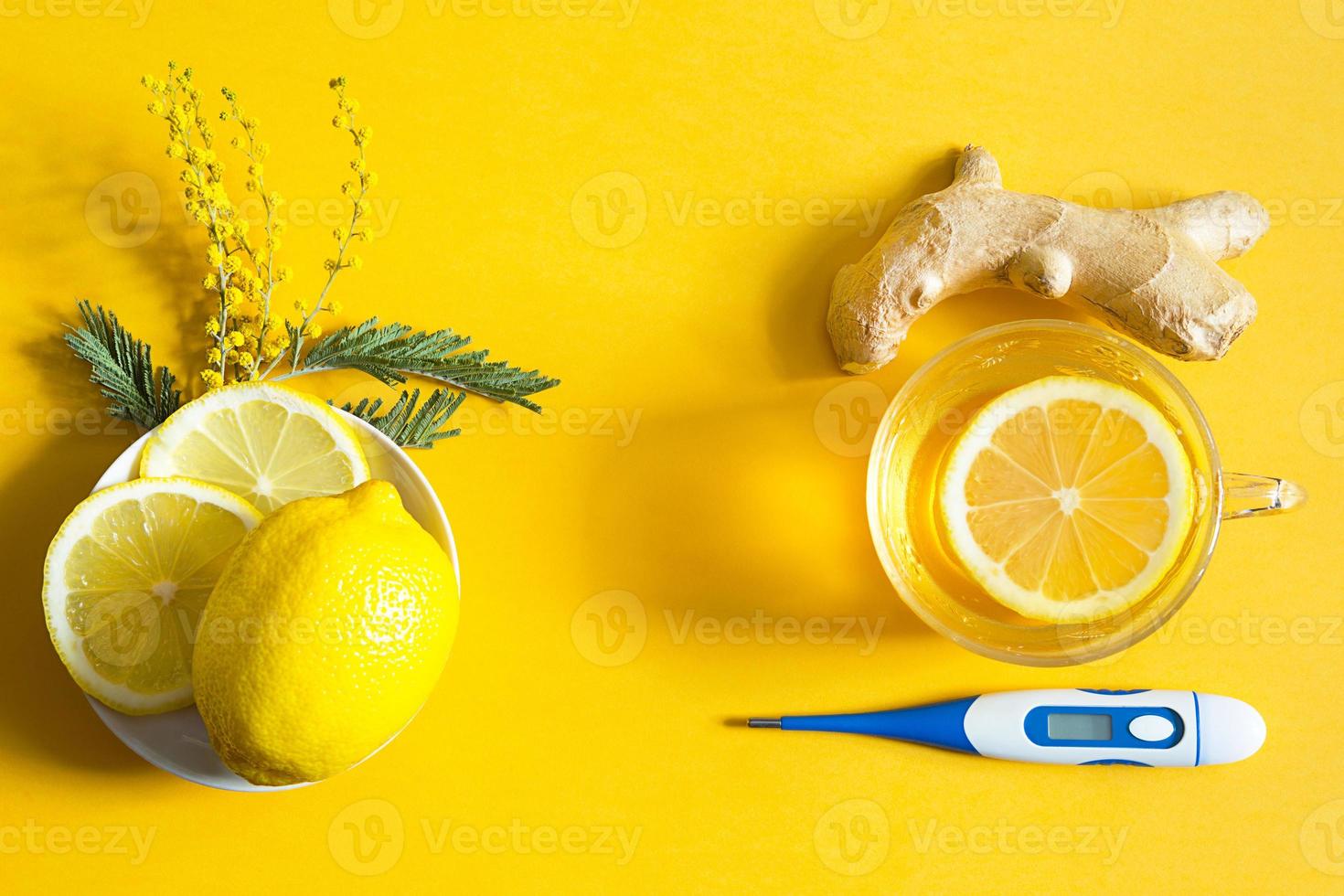Medicinal tea in a cup, ginger, lemon, acacia-strengthen the immune system in cold season, thermometer and copy space, sheet for notes. Vitamin drink for health and ingredients on yellow background. photo