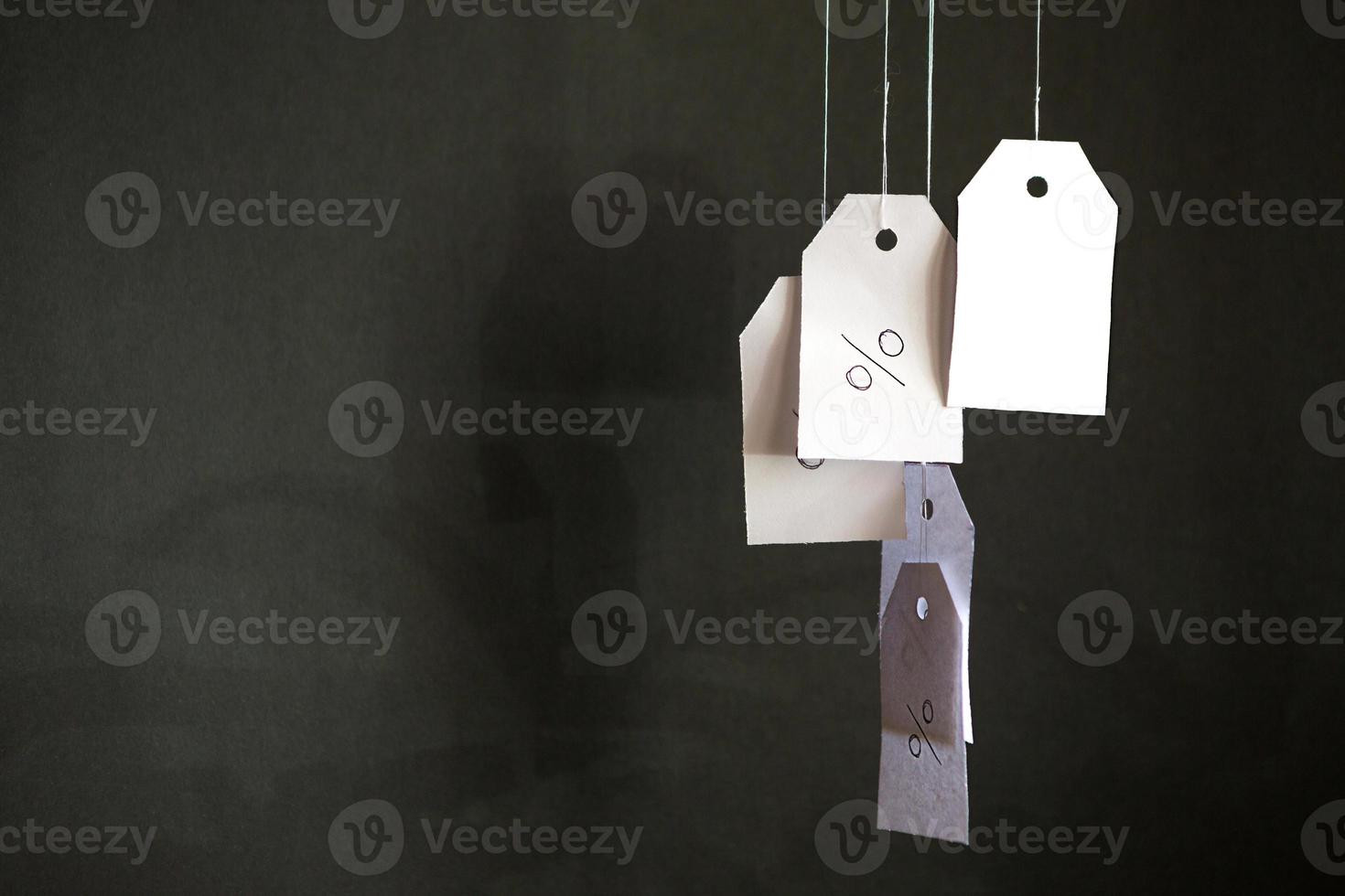 White tags with the percent sign hang on strings on a black background with shadows. Commerce, discount, sale, trade offer. Copy space, mock up. Black Friday photo