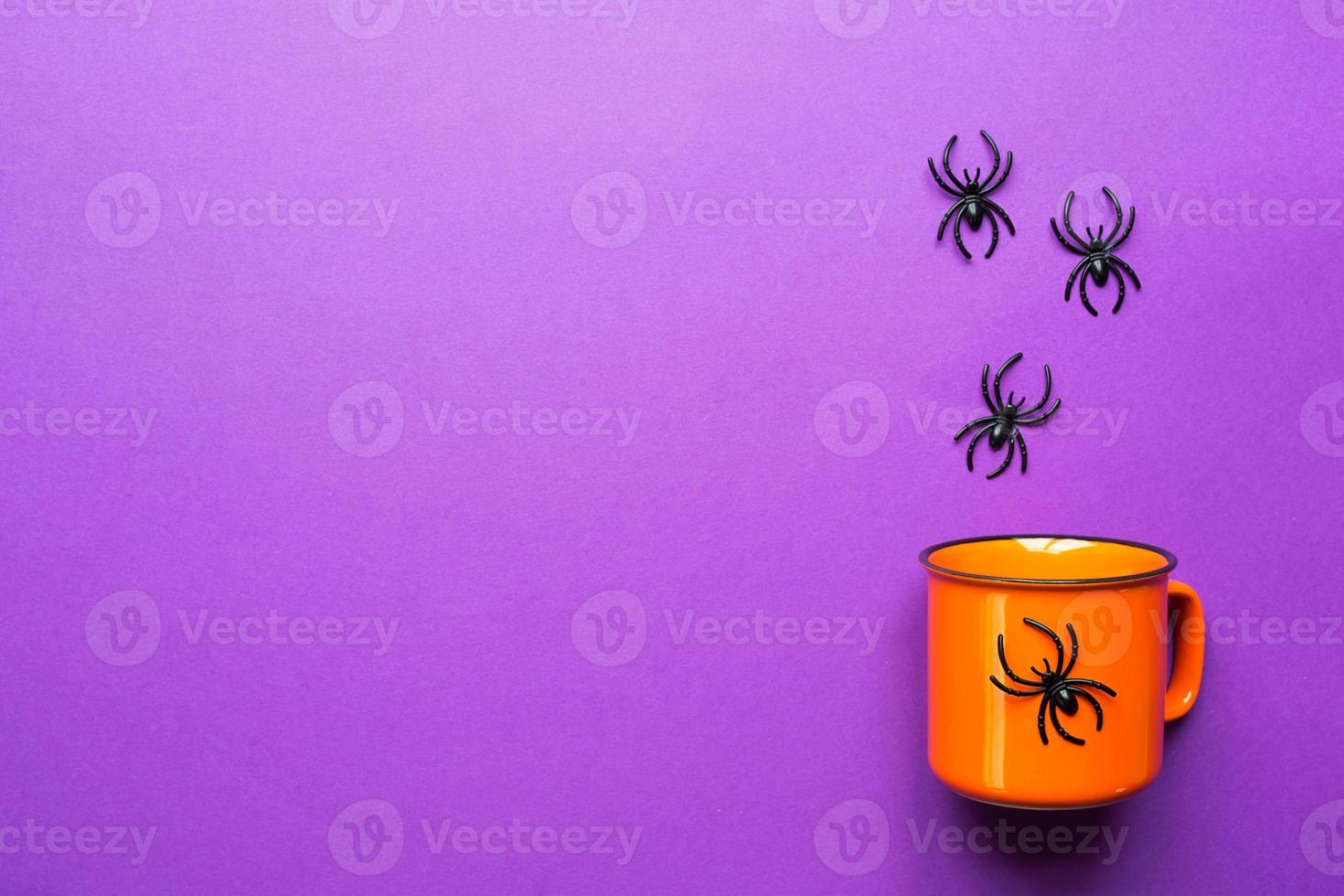 Orange mug on a purple background with spiders. The concept of the Halloween holiday. Terrible scenery, terrible drink, fun. Copy space, mock up, flatly photo