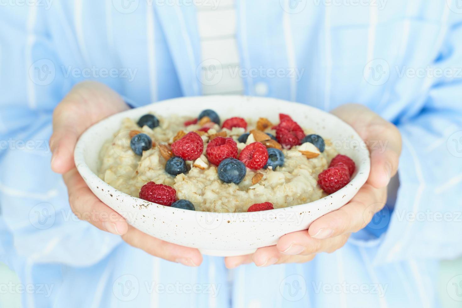 Faceless woman holds in hands breakfast, oatmeal porridge with berries and nuts photo