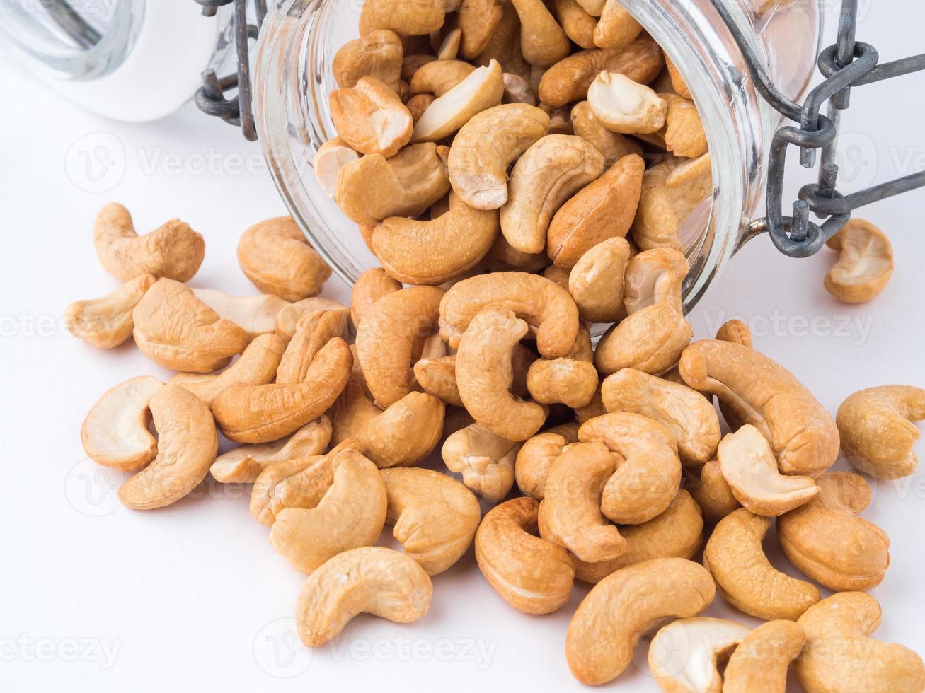 Glass bottle with cashew nuts on white background. A glass bowl with a scattering of nuts, side view, photo