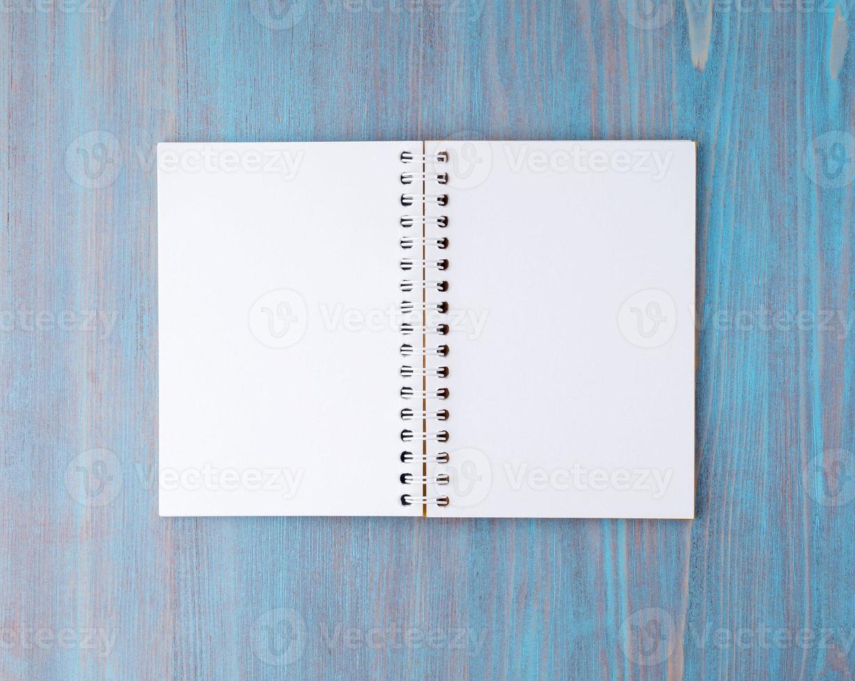 Open notebook on spring with white paper for notes and drawing. Light background, blue wood, top view. photo