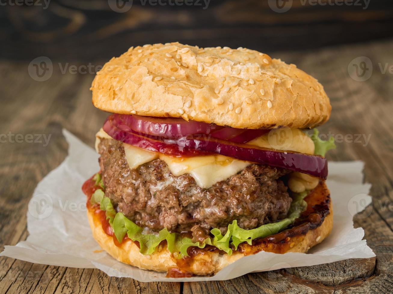 Big delicious homemade burger with beef cutlet, cheese, onion, tomato and lettuce on toasted rolls. American fast food, unhealthy eating. Side view, selective focus photo