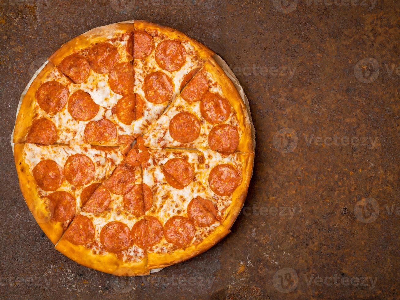 round Italian pizza pepperoni on a rusty metal desk top view, empty space for text. photo