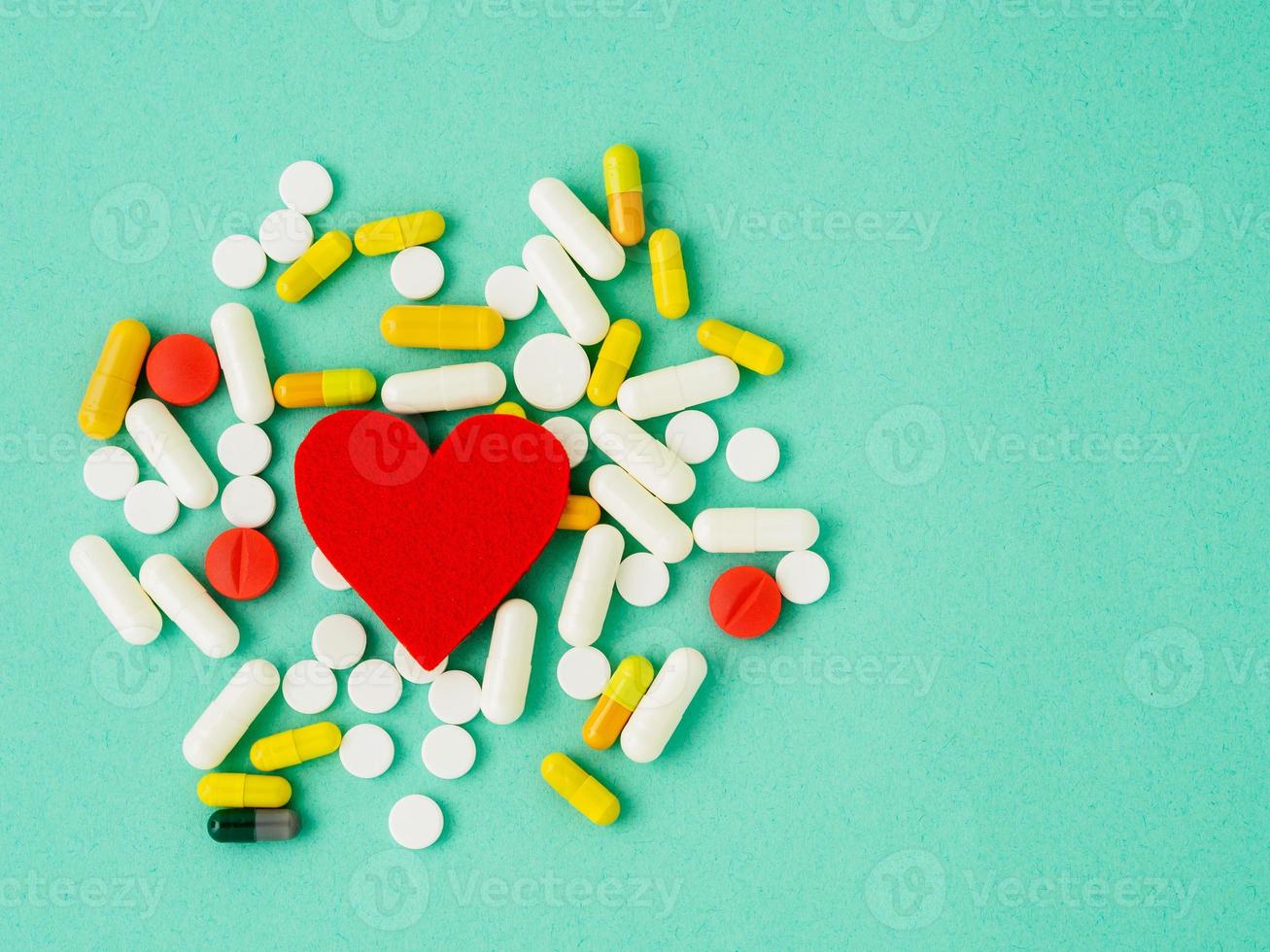 handful of pills and a red heart on a bright turquoise blue colour table, top view, copy space. Medicine help for heart health. photo