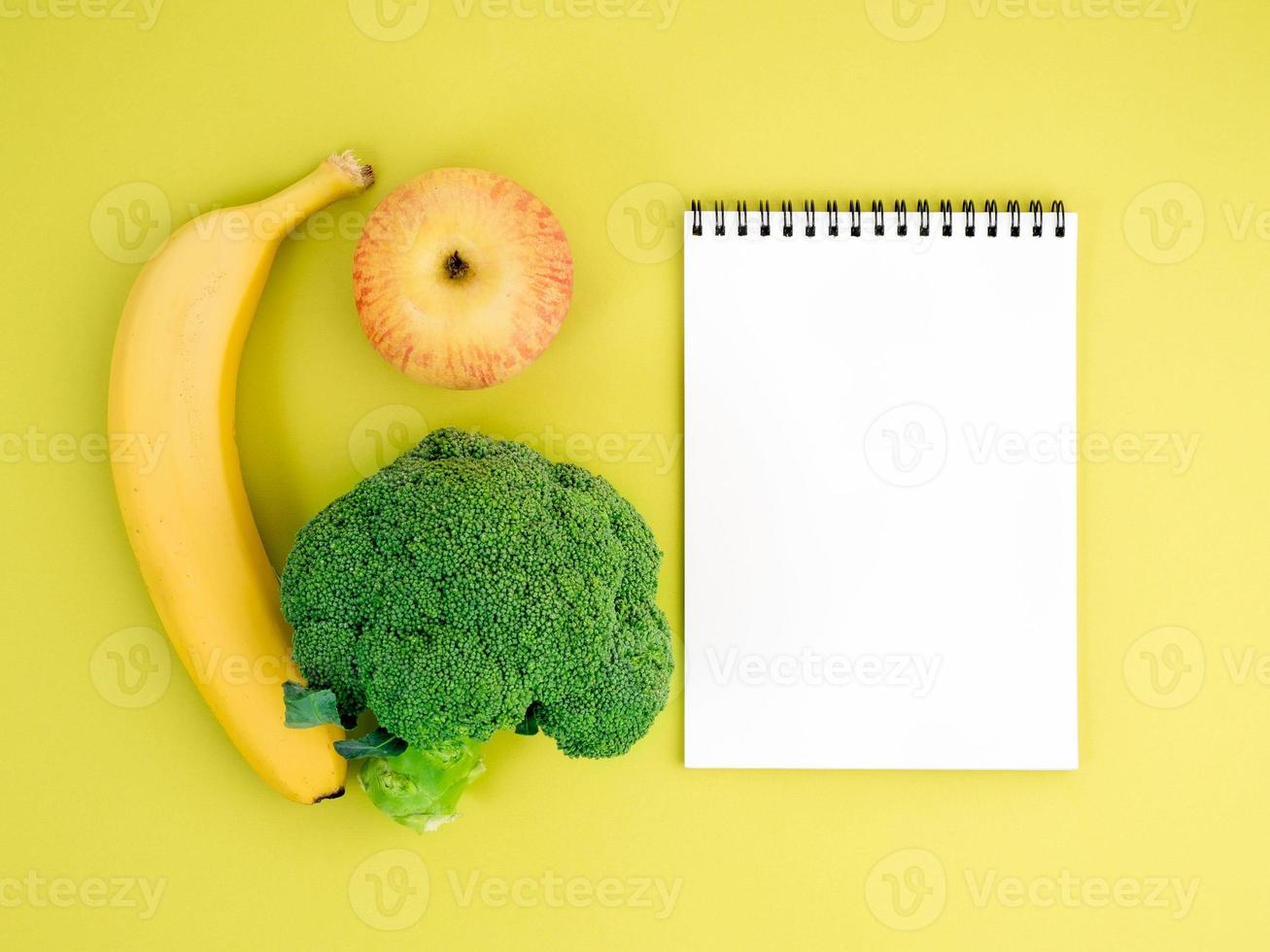 frutas y verduras - manzana, plátano y brócoli sobre fondo amarillo brillante. cuaderno para registrar sobre nutrición adecuada, vitaminas, estilo de vida saludable. foto