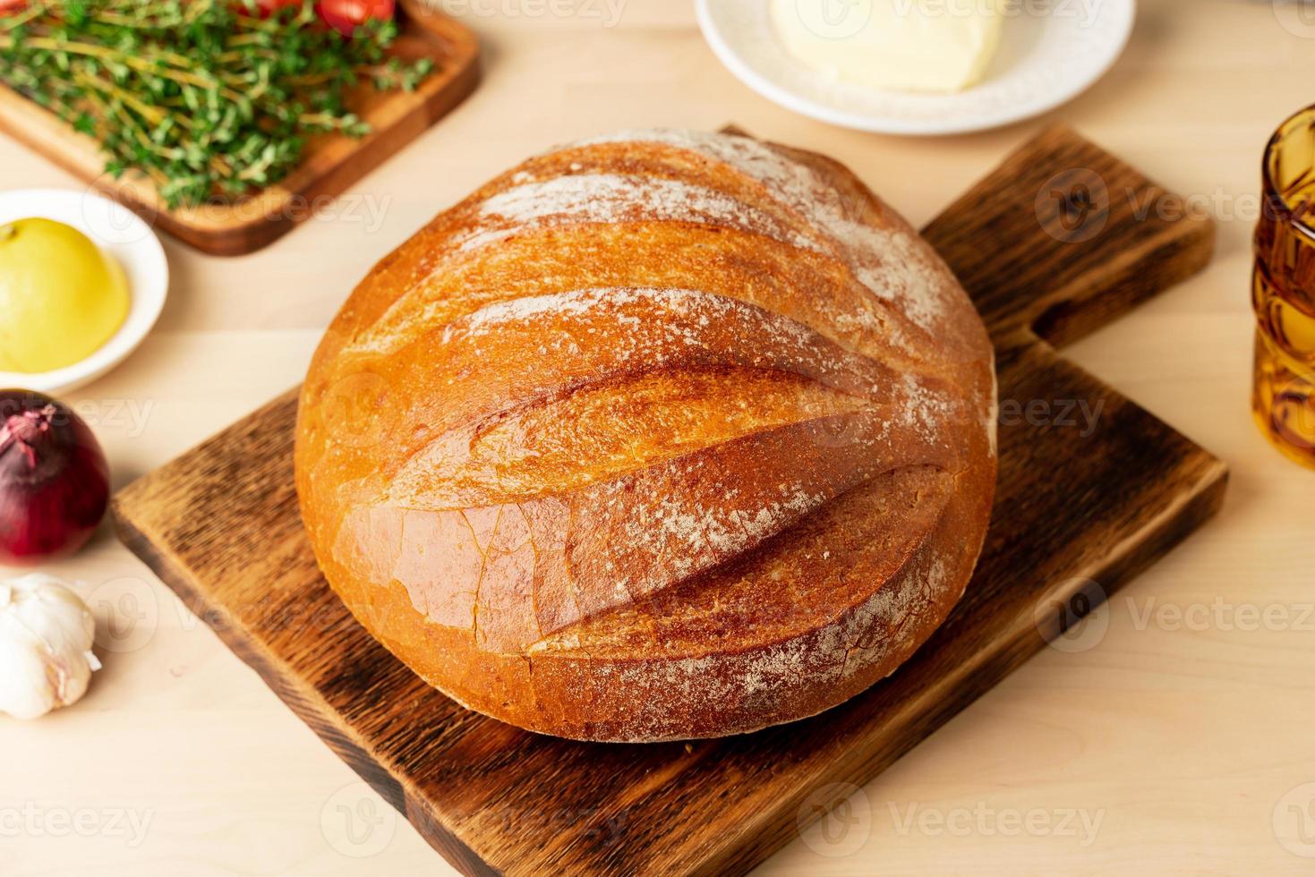 Whole loaf of freshly baked white wheat bread on wooden board on home kitchen table photo