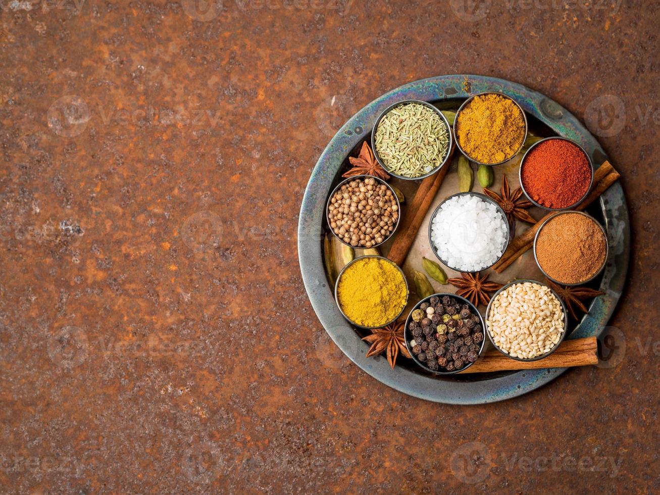 Mix spices on round metal plate - coriander, pepper, salt, rosemary, turmeric, curry. Top view, close up, copy space, metall rusty background. photo