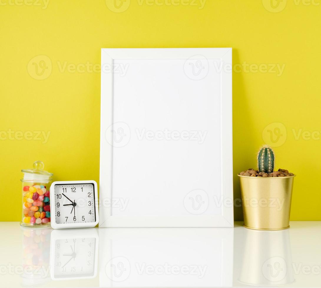 Blank white frame, clock, succulent, candy on white table agains photo