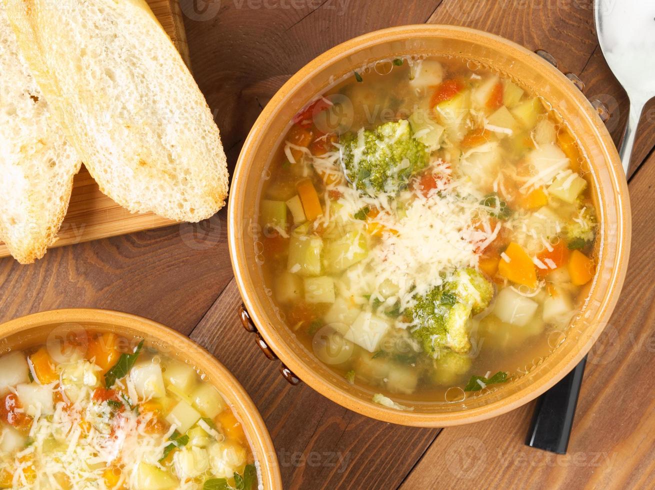 Two bowl of minestrone soup with toast on rustic wooden background, top view, close up photo