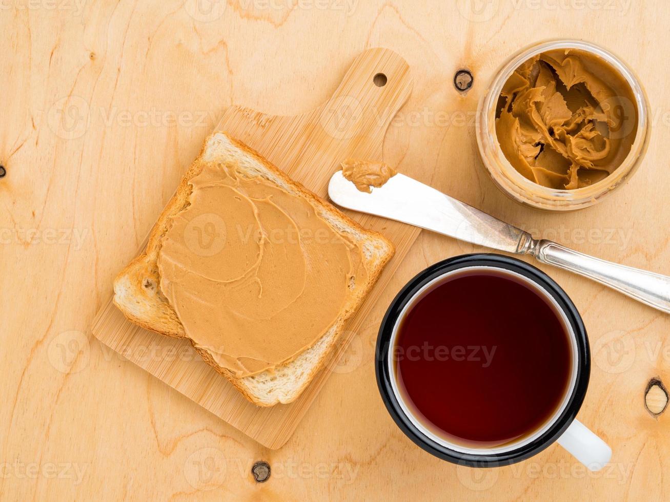 toast with peanut butter, knife for spreading on a sandwich, a mug of tea on a beige wood background photo