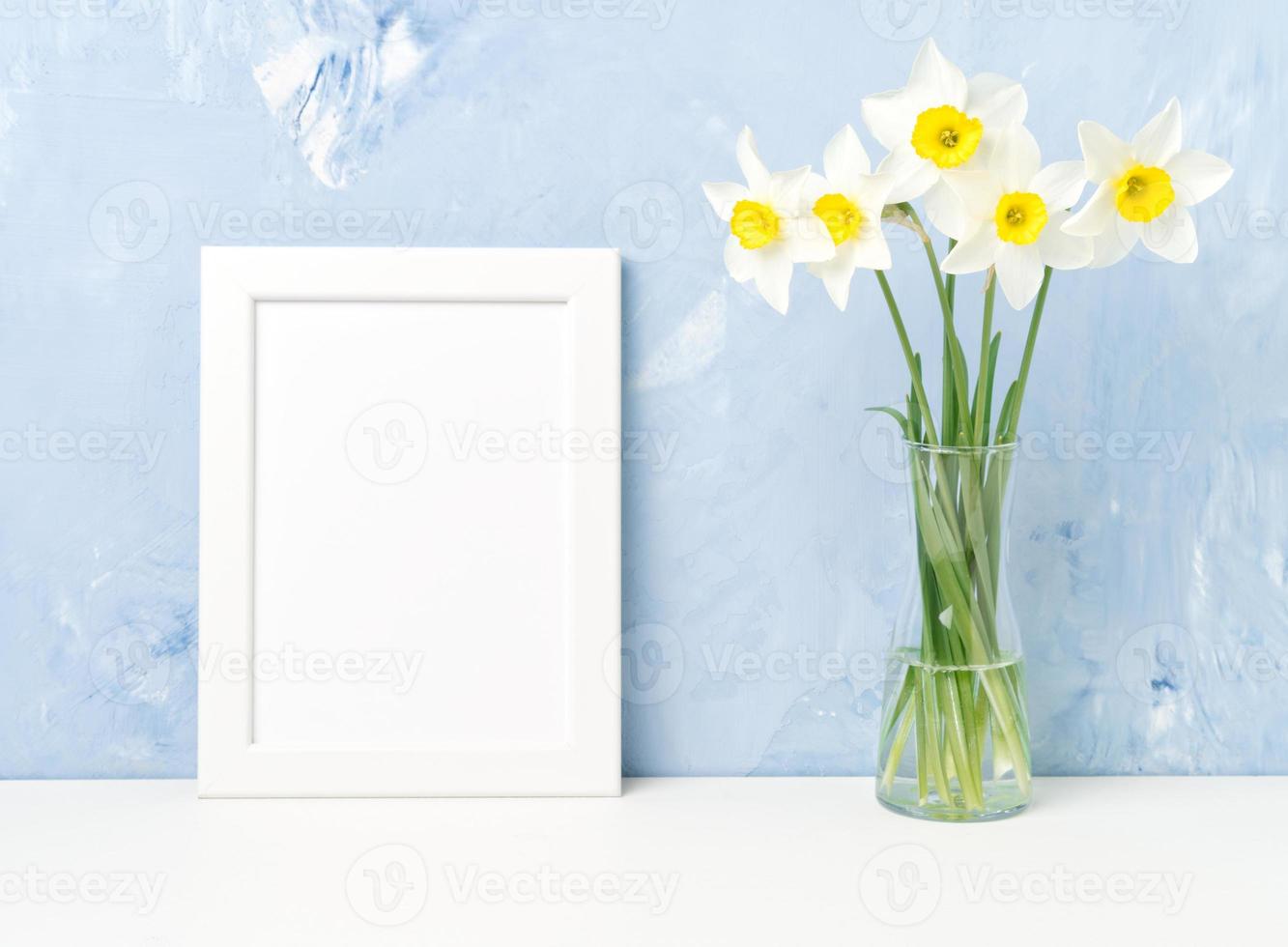 Bouquet of fresh flowers, white frame on table, opposite blue textured concrete wall photo