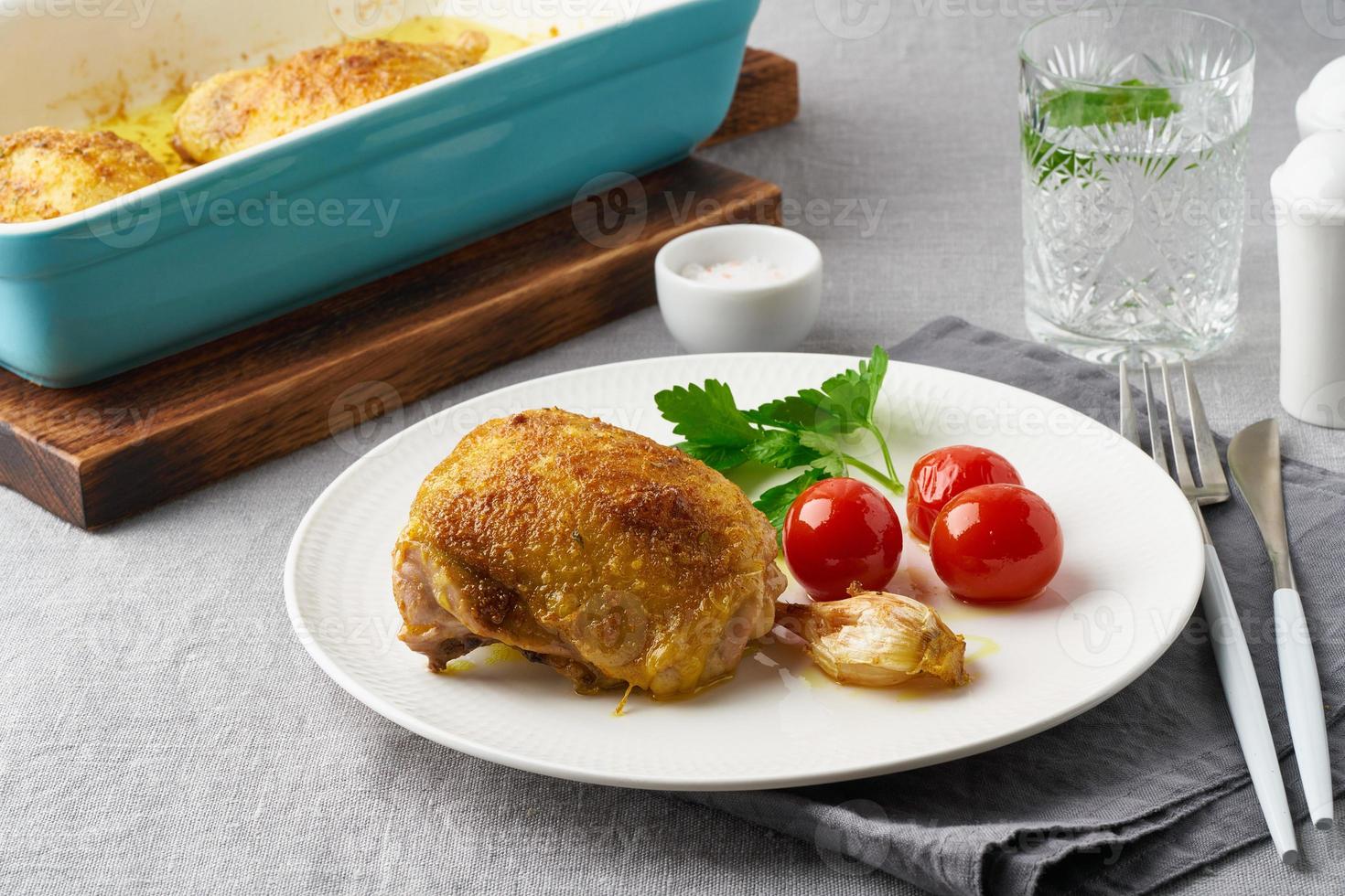 Chicken thighs baked with turmeric, tomatoes and garlic. Fried chicken is on plate photo