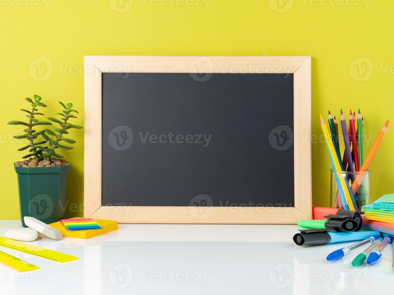 Chalkboard, succulent and school supplies by the yellow wall. Side view, empty space for text. Back to school concept. photo
