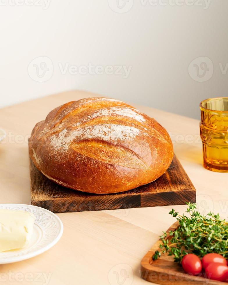 toda la hogaza de pan de trigo blanco recién horneado en una tabla de madera en la mesa de la cocina casera foto