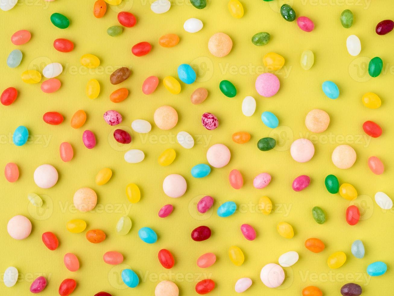 Many scattered colorful sweets, candies, lollipops on bright yellow background, top view photo