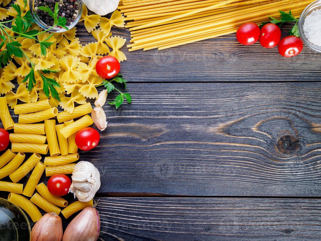 pasta, tomatoes, shallots, garlic, parsley on dark wooden background, top view, copy space. photo