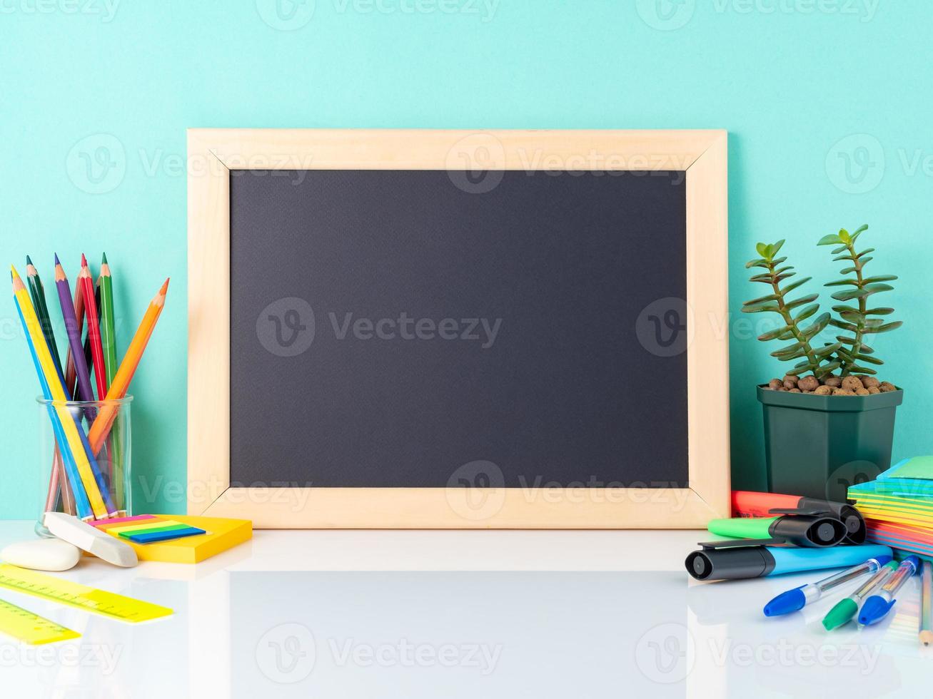 Chalkboard and school supplies on white table by the blue wall. Side view, empty space. Back to school concept. photo