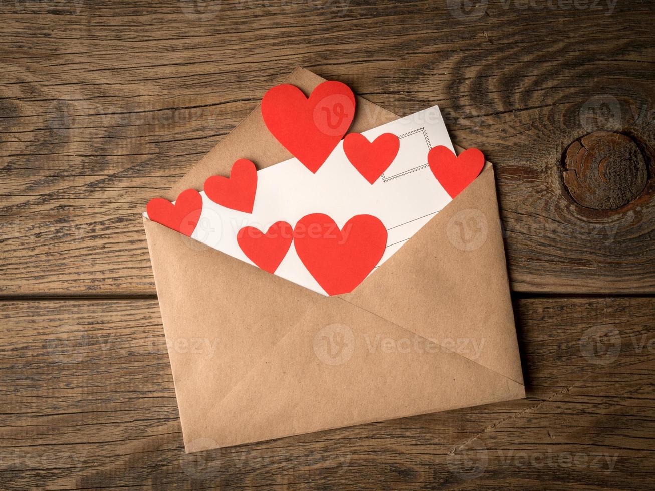 card and red hearts in open envelope from brown Kraft paper on wooden aged vintage background. Greetings with Valentine's day photo