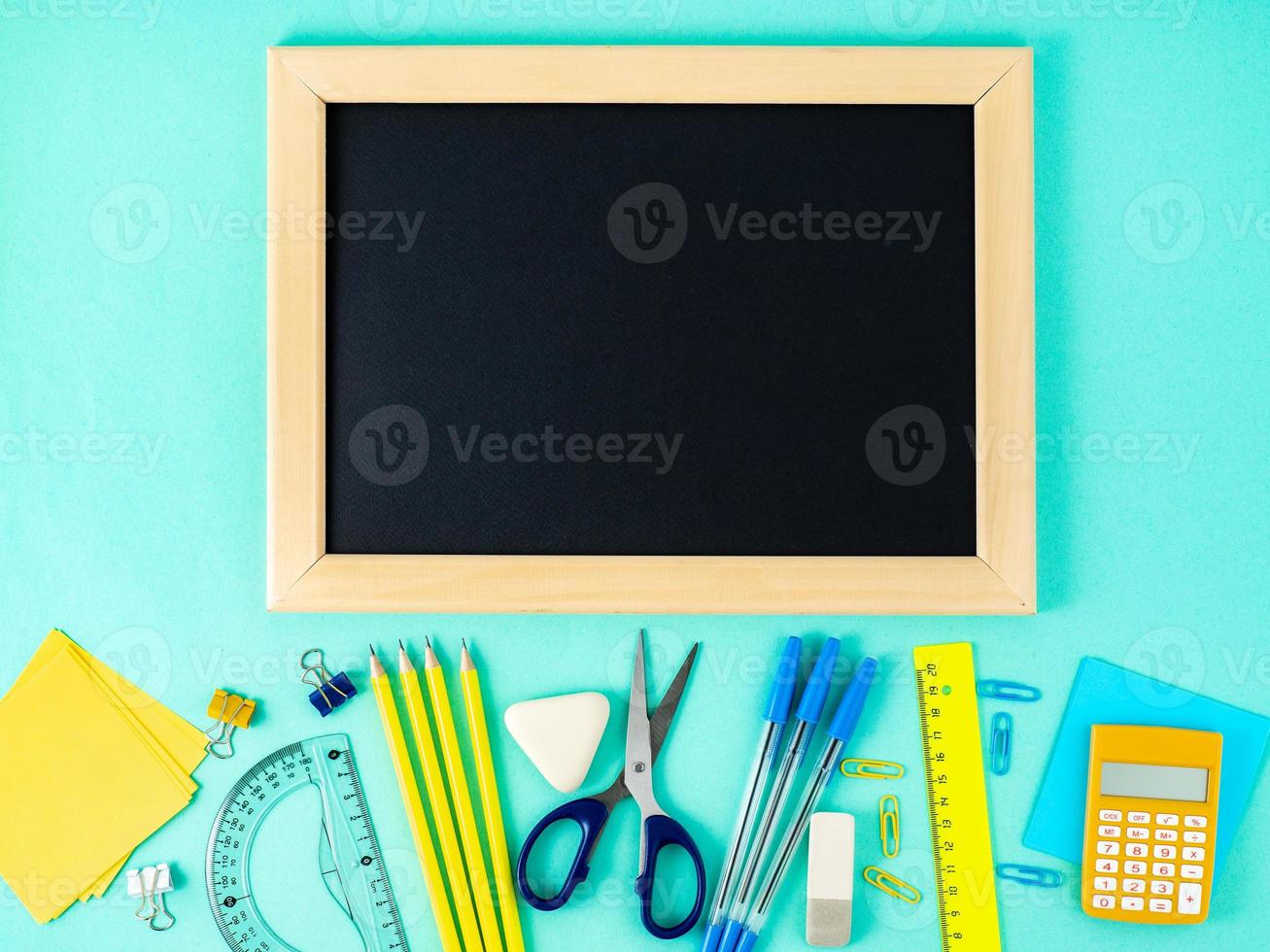 Chalkboard and school supplies on white table by the blue wall. Top view, flat lay, empty space. Back to school concept. photo