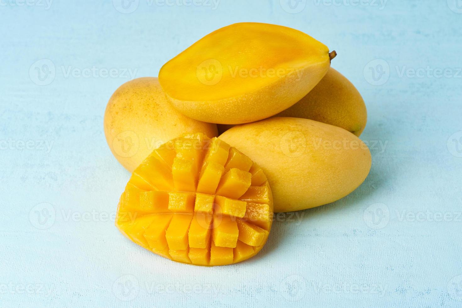 cuatro frutas enteras de mango sobre una mesa azul brillante y cortadas en rodajas. frutos amarillos grandes y jugosos foto