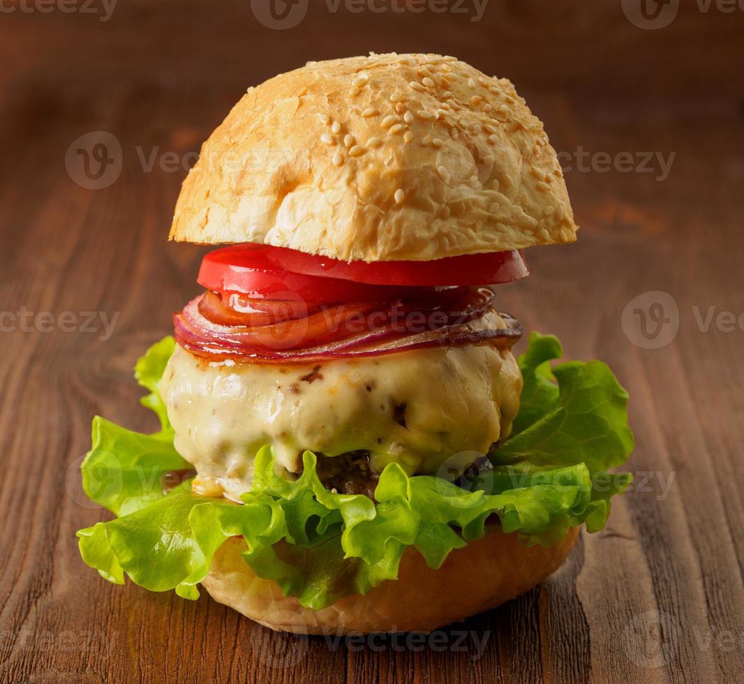 Big delicious homemade burger with beef cutlet, cheese, onion, tomato and lettuce on toasted rolls. American fast food, unhealthy eating. Side view, selective focus photo