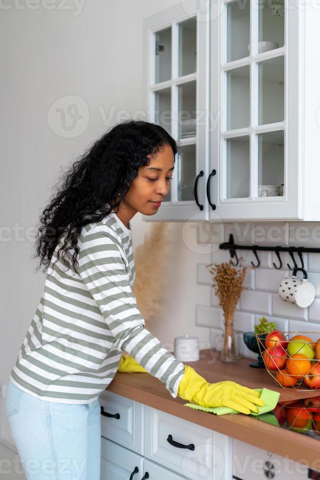 mujer afroamericana ocupada con tareas domésticas en la cocina. usando guantes de goma amarillos foto