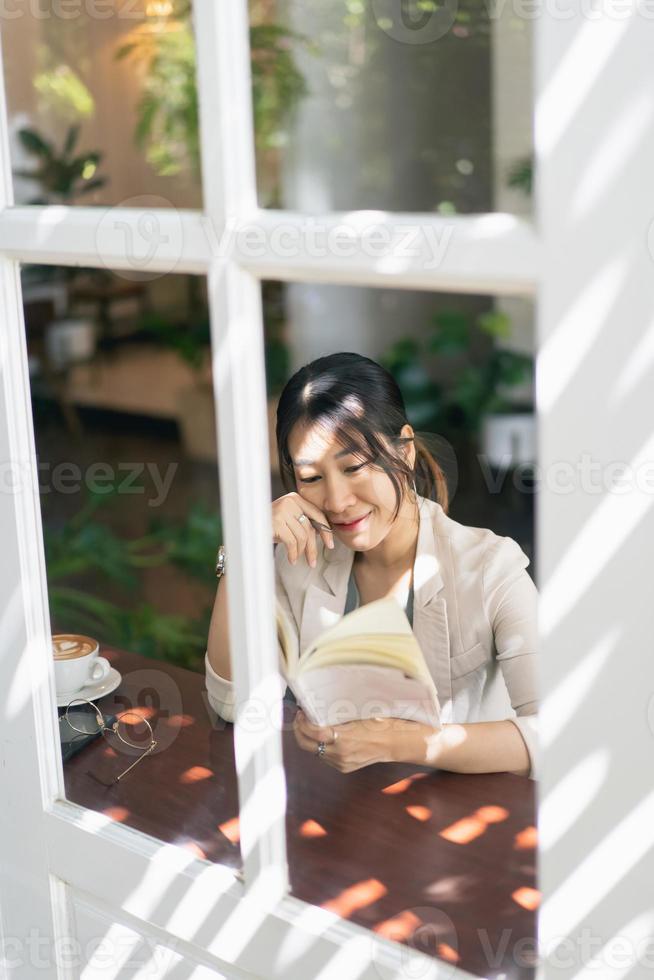 Woman wearing watches and writing journal on small notebook at indoor cafe. Woman notes and drinking coffee at cafe. View from window in cafe. photo