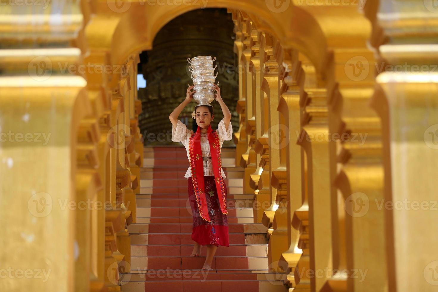 joven asiática con traje tradicional birmano sosteniendo un tazón de arroz a mano en la pagoda dorada en el templo de myanmar. mujeres de myanmar sosteniendo flores con vestido tradicional birmano visitando un templo budista foto