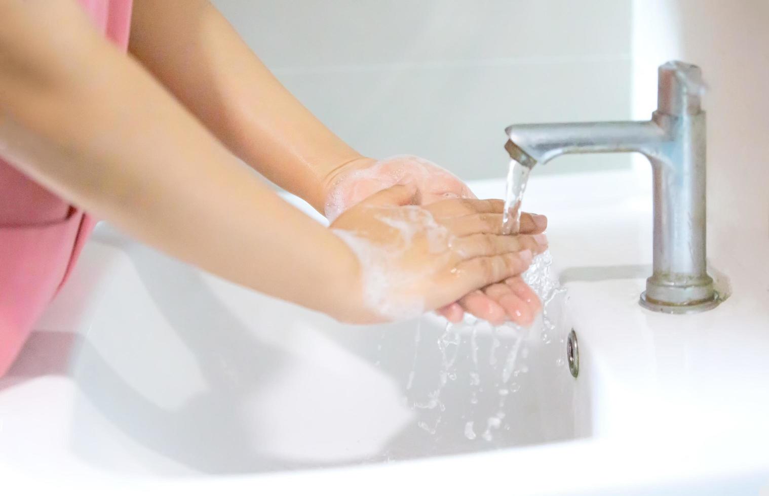 Hygiene. Cleaning Hands. Washing hands with soap. Young woman washing hands with soap over sink in bathroom, closeup. Covid19. Coronavirus. photo