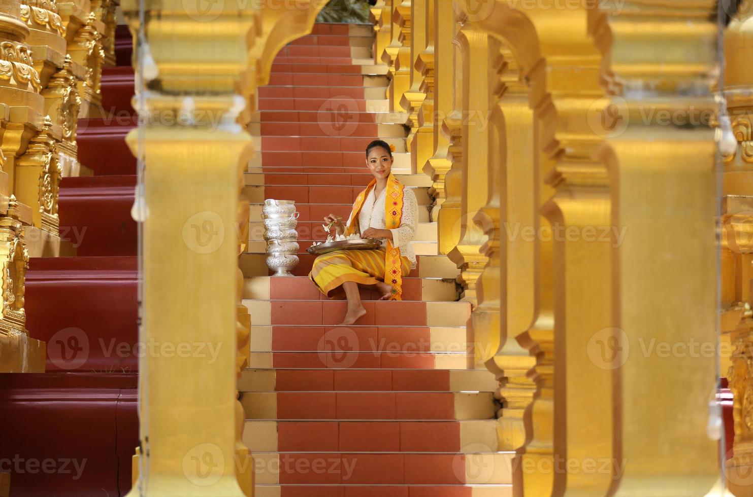 Young Asian girl in traditional Burmese costume holding bowl of rice on hand at golden pagoda in Myanmar temple. Myanmar women holding flowers with Burmese traditional dress visiting a Buddhist temple photo